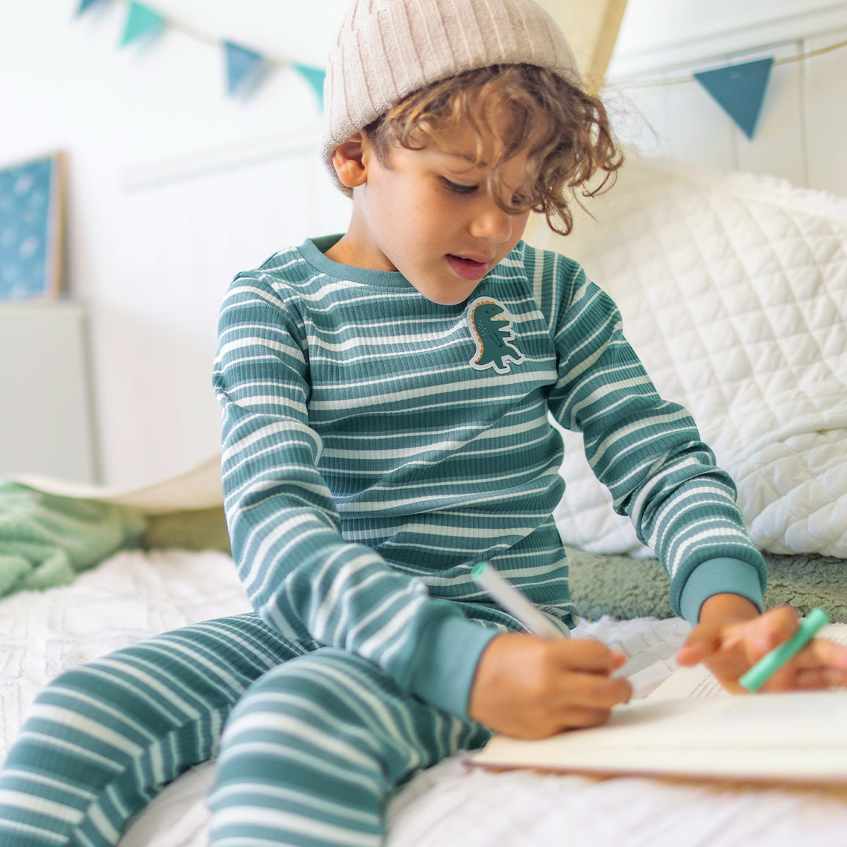 Enfant portant le pyjama deux pièces vert à rayures en coton côtelé, assis sur un lit