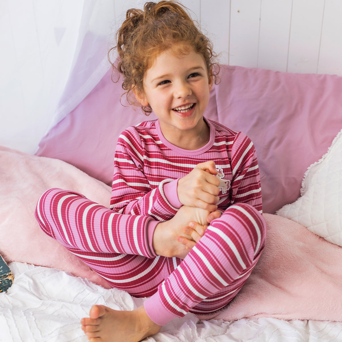 Enfant portant le pyjama deux pièces rose à rayures en coton côtelé, assis sur un lit
