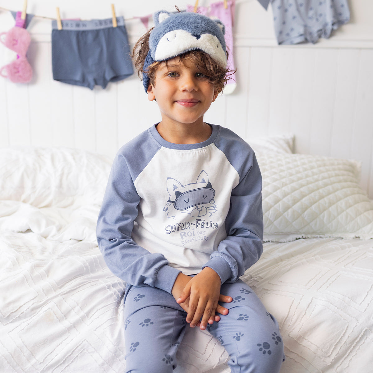 Enfant portant le pyjama deux pièces bleu à illustration de chat en coton doux, assis sur un lit avec un masque de sommeil en forme de chat assorti