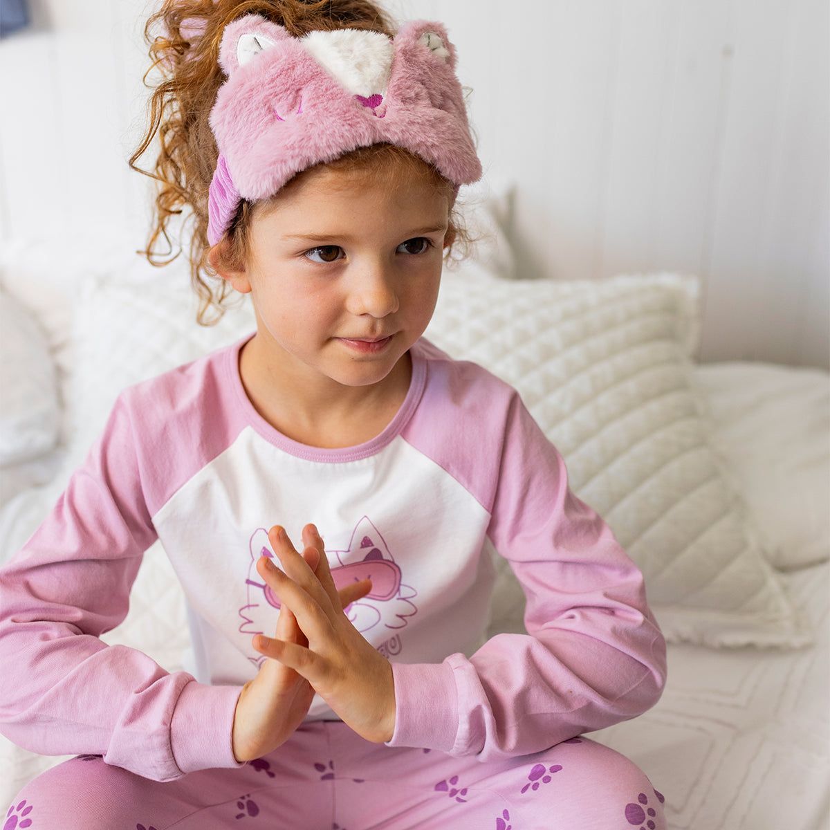 Enfant portant le pyjama deux pièces rose à illustration de chat en coton doux, assis sur un lit avec un masque de sommeil en forme de chat assorti
