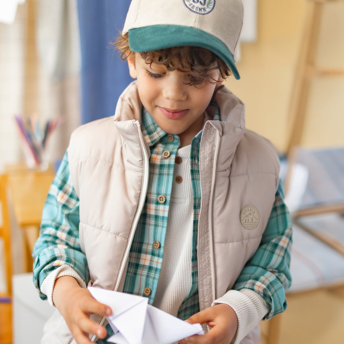 Chemise verte à carreaux en flanelle de coton pour enfant à manches longues avec boutons effet bois, portée sous une veste sans manches matelassée crème.