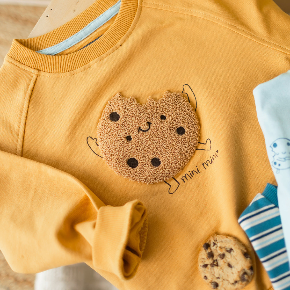 Chandail jaune ocre en coton français pour bébé à manches longues avec illustration texturée en bouclette d'un biscuit sur le devant.