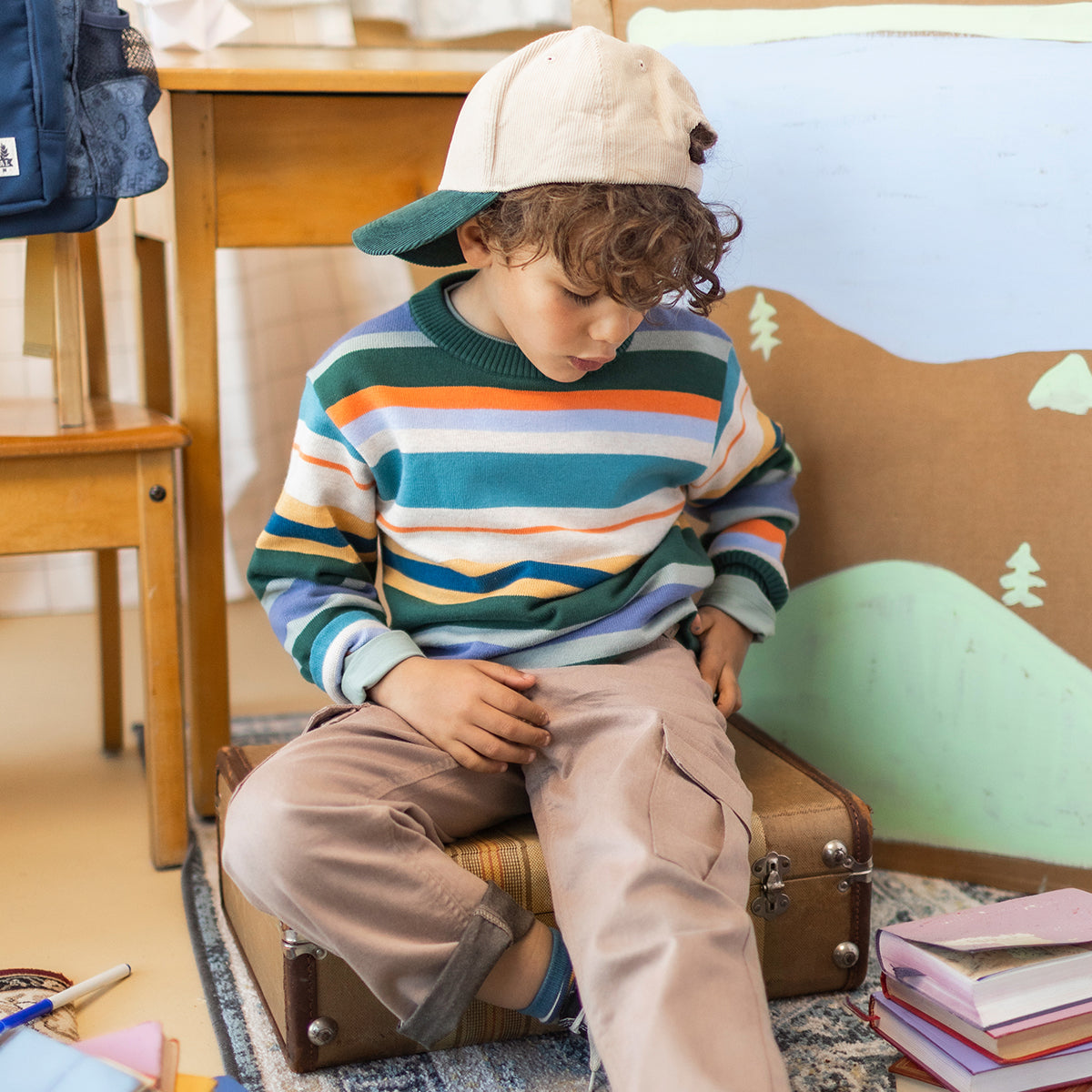 Chandail de maille rayé pour enfant à manches longues avec rayures vertes, bleues, blanches et orange, porté par un enfant avec une casquette.
