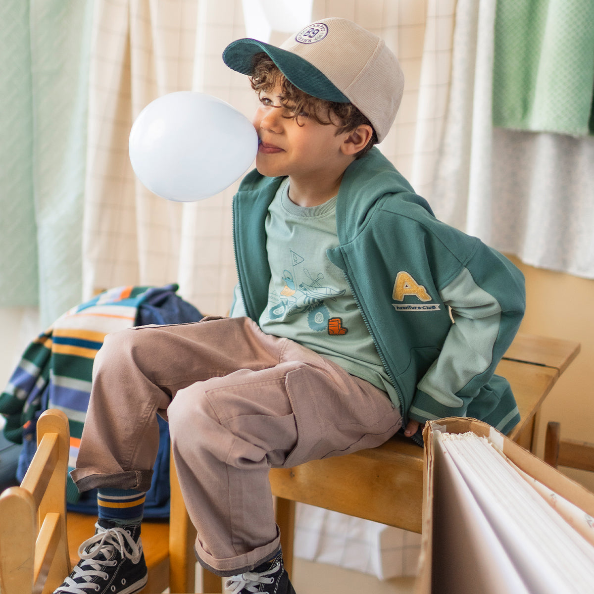 Veste verte en coton ouaté pour enfant avec capuchon, fermeture à glissière et écusson brodé à l'avant, portée par un enfant.