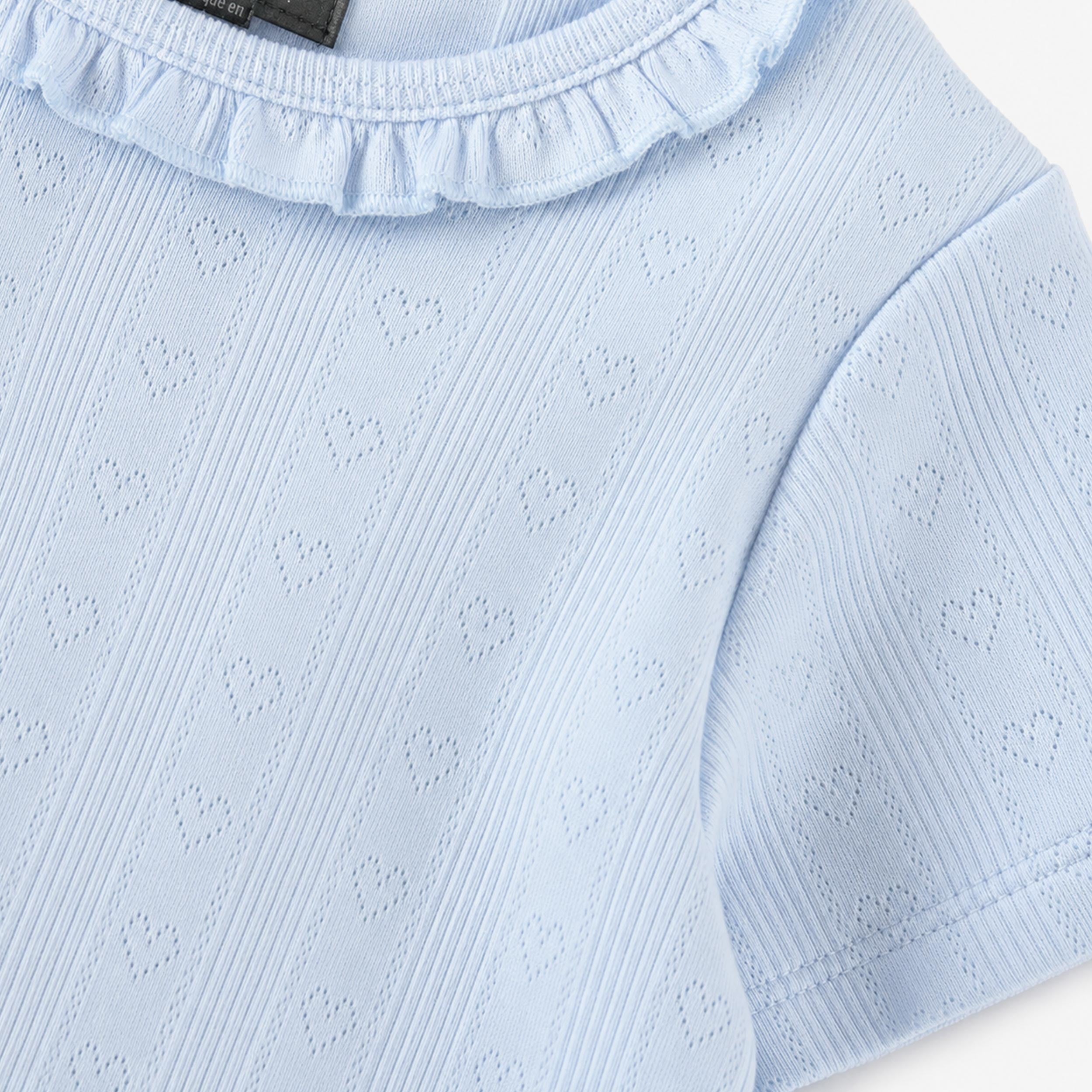 T-shirt bleu pâle pour bébé fille avec texture ajourée à motifs cœurs et col volanté. Doux, confortable et idéal pour tous les jours.