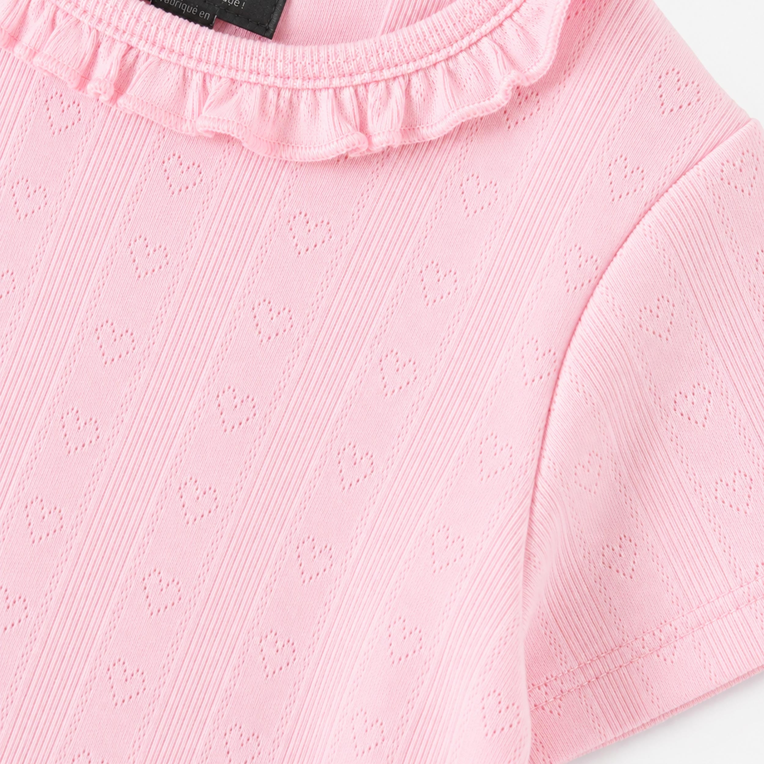 T-shirt rose pour bébé fille avec texture ajourée à motifs cœurs et col volanté. Doux, confortable et parfait pour un look délicat.