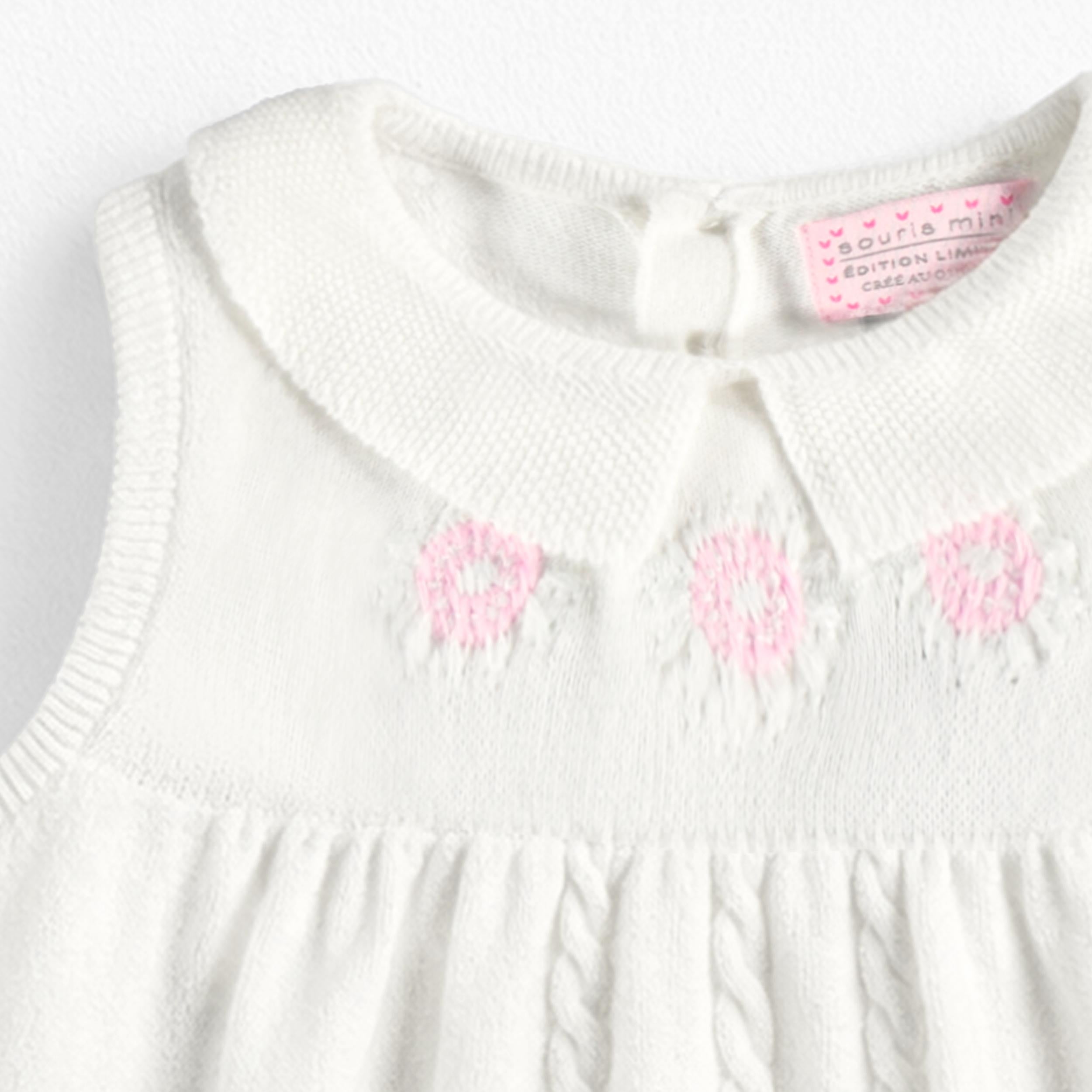 Zoom détails broderies de la robe blanche en tricot avec broderies de fleurs, bébé