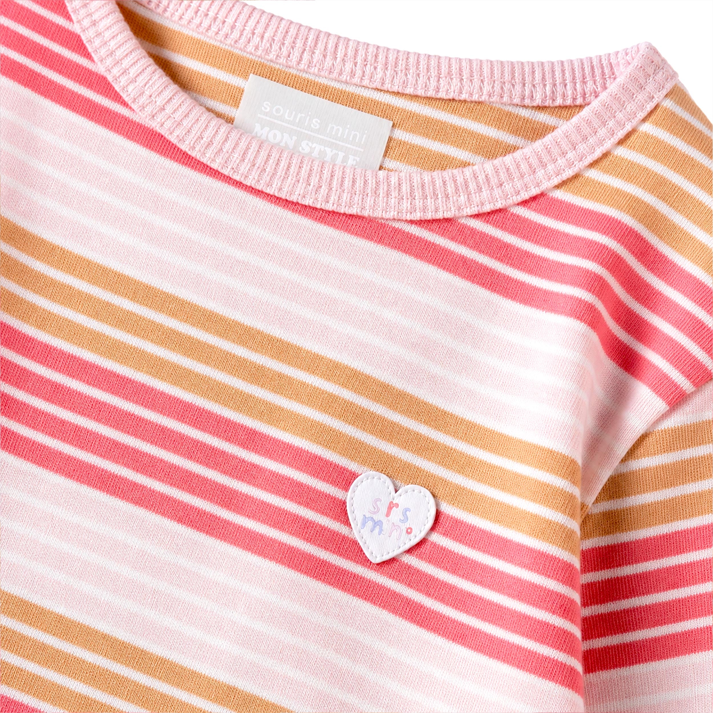 Gros plan sur un chandail à manches longues pour bébé fille à rayures rose, rose pâle et caramel avec encolure rose et écusson cœur décoratif.