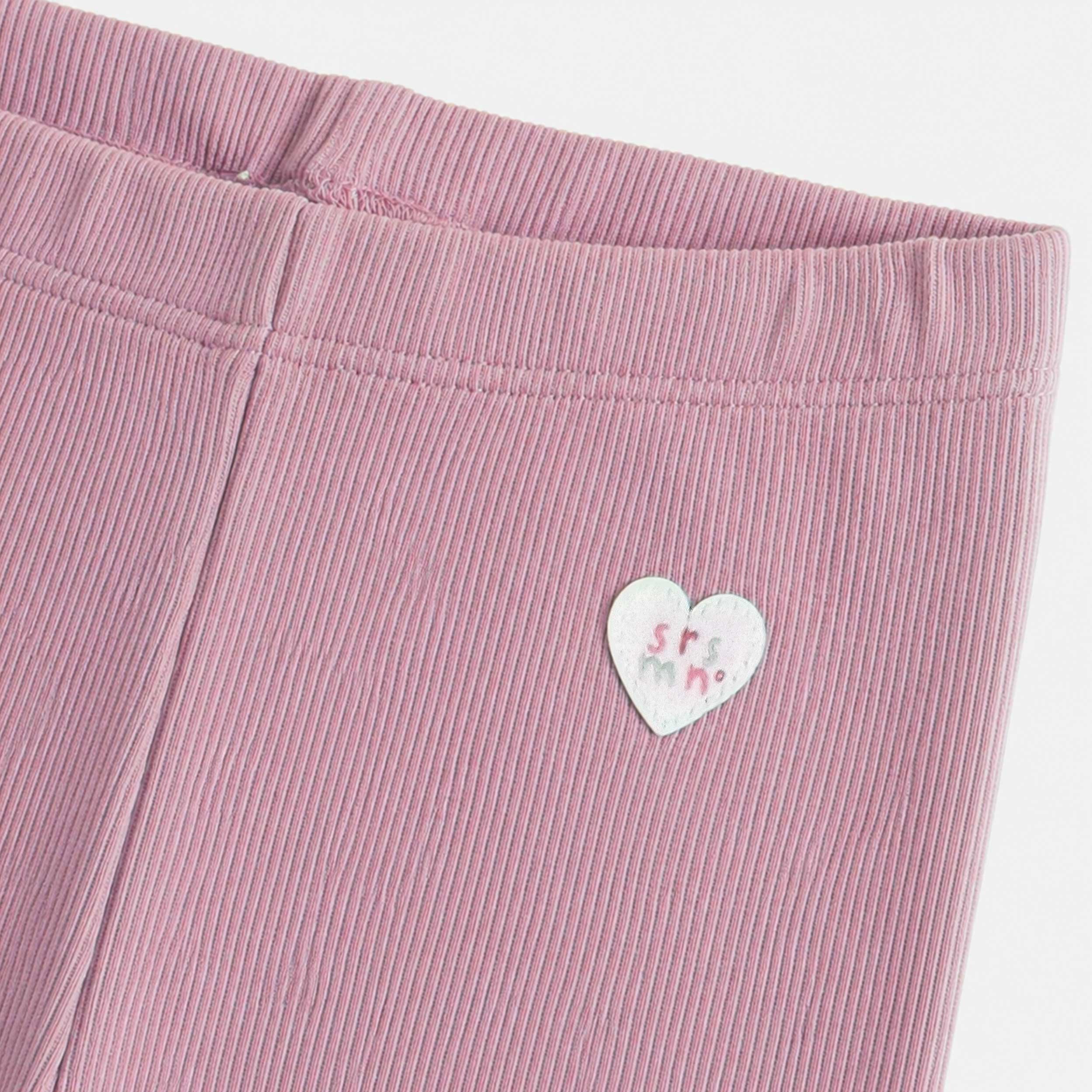 Gros plan sur un legging côtelé rose mauve pour bébé fille, mettant en valeur la taille élastique confortable et l’écusson cœur décoratif.