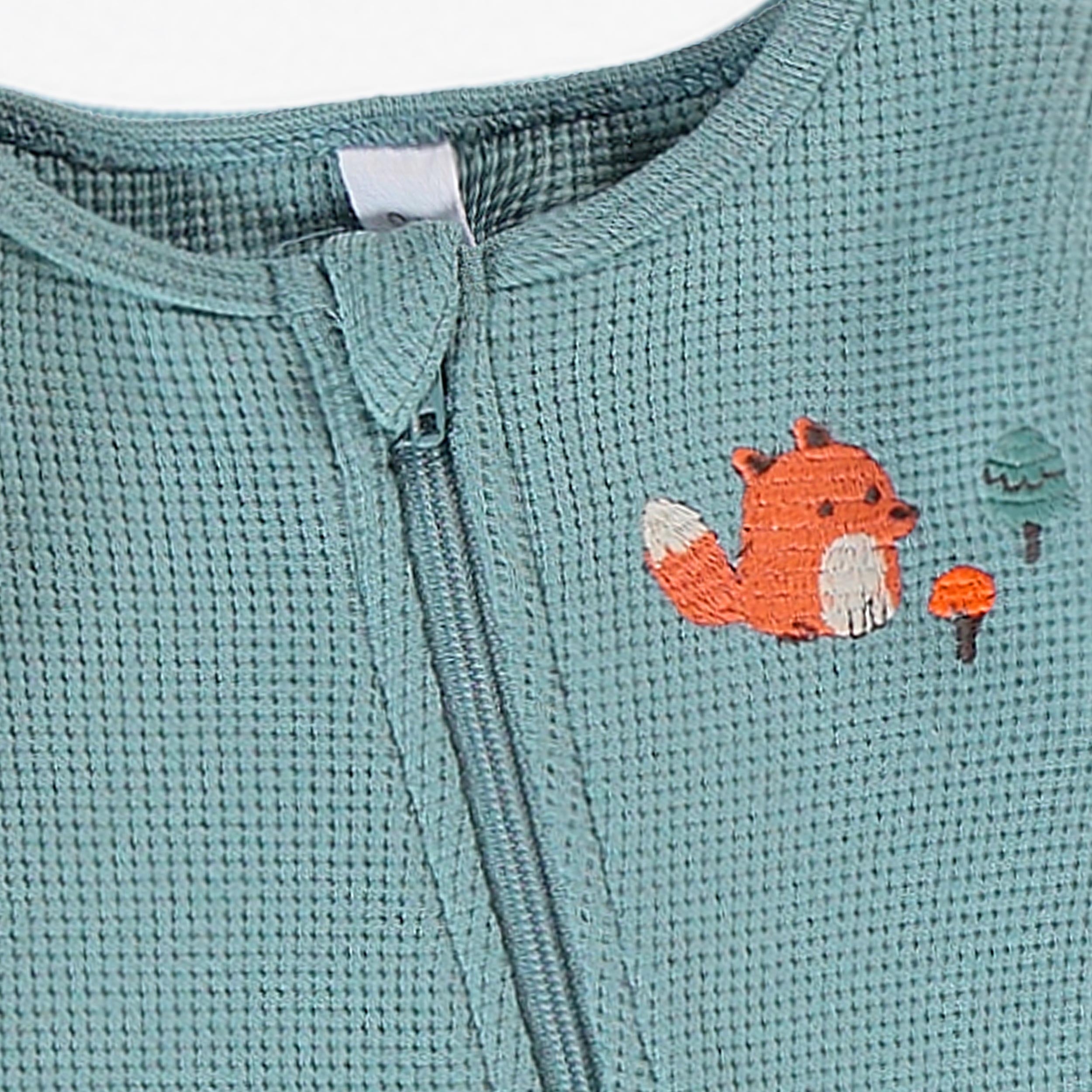 Gros plan sur le pyjama gaufre vert sauge pour bebe garcon avec fermeture eclair et broderie renard sur la poitrine.