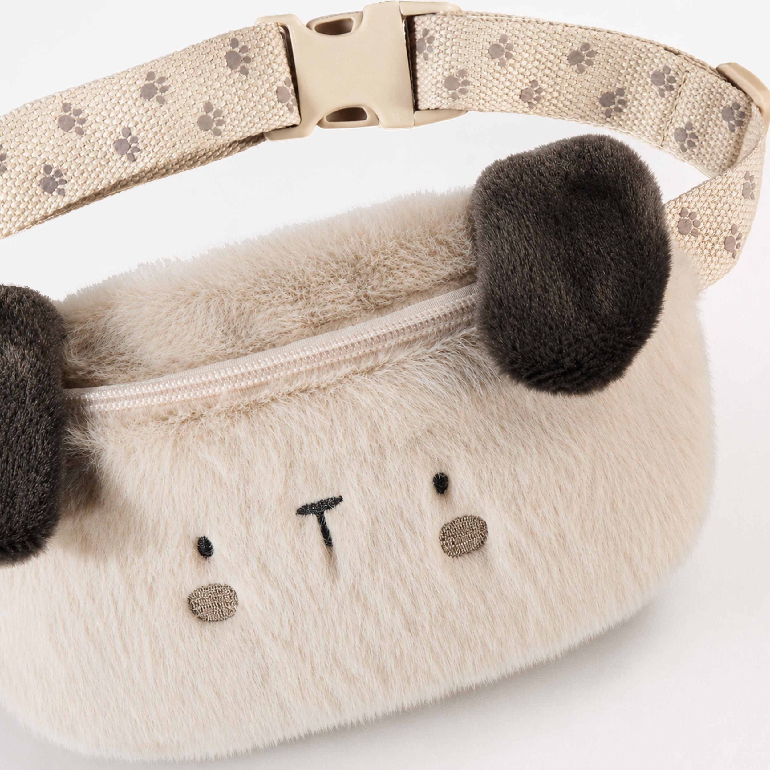 Gros plan sur un sac banane en peluche beige pour enfant avec visage d’ours brodé, oreilles en relief, fermeture à glissière et sangle ajustable à motif floral.