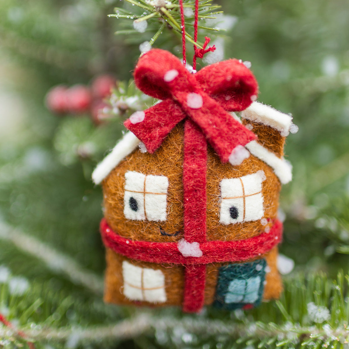 Décoration de Noël Souris Mini en feutre représentant une maison pain d’épice ornée d’un grand nœud rouge suspendue dans le sapin.
