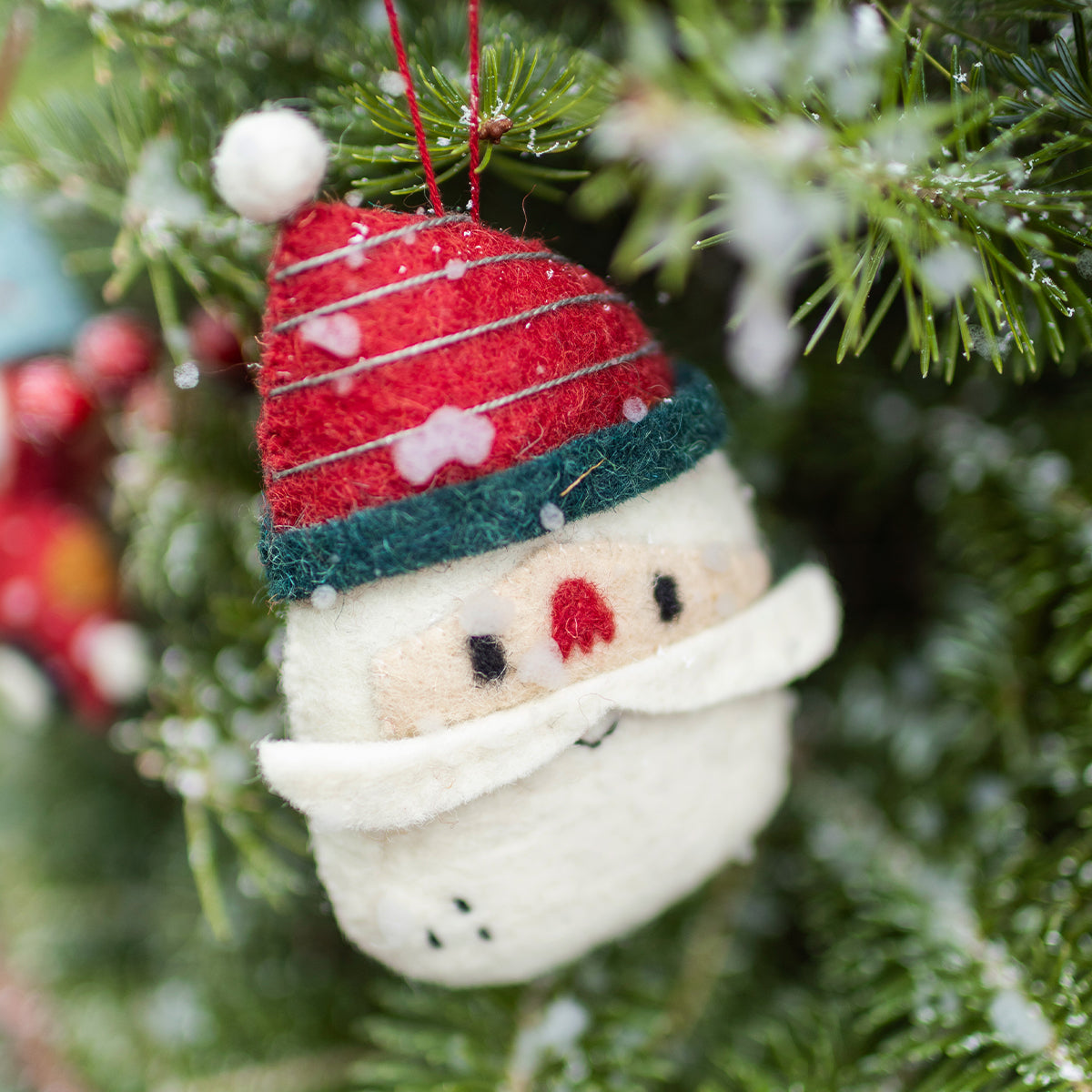 Décoration de Noël Souris Mini en feutre représentant un Père Noël avec bonnet rouge et vert accrochée dans un sapin enneigé.