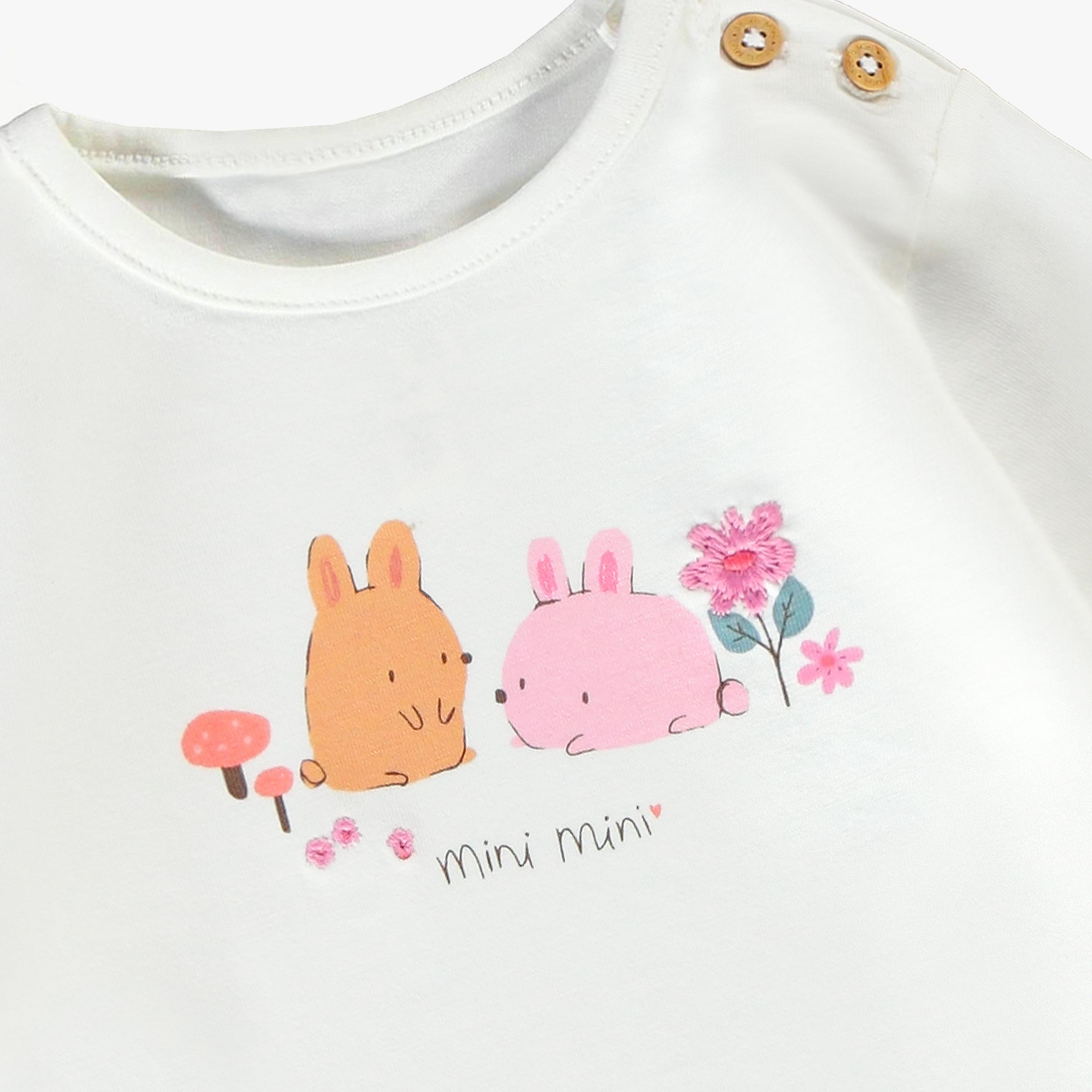 Gros plan sur le motif de deux lapins et fleurs brodées d’un t-shirt bébé fille blanc à manches longues.