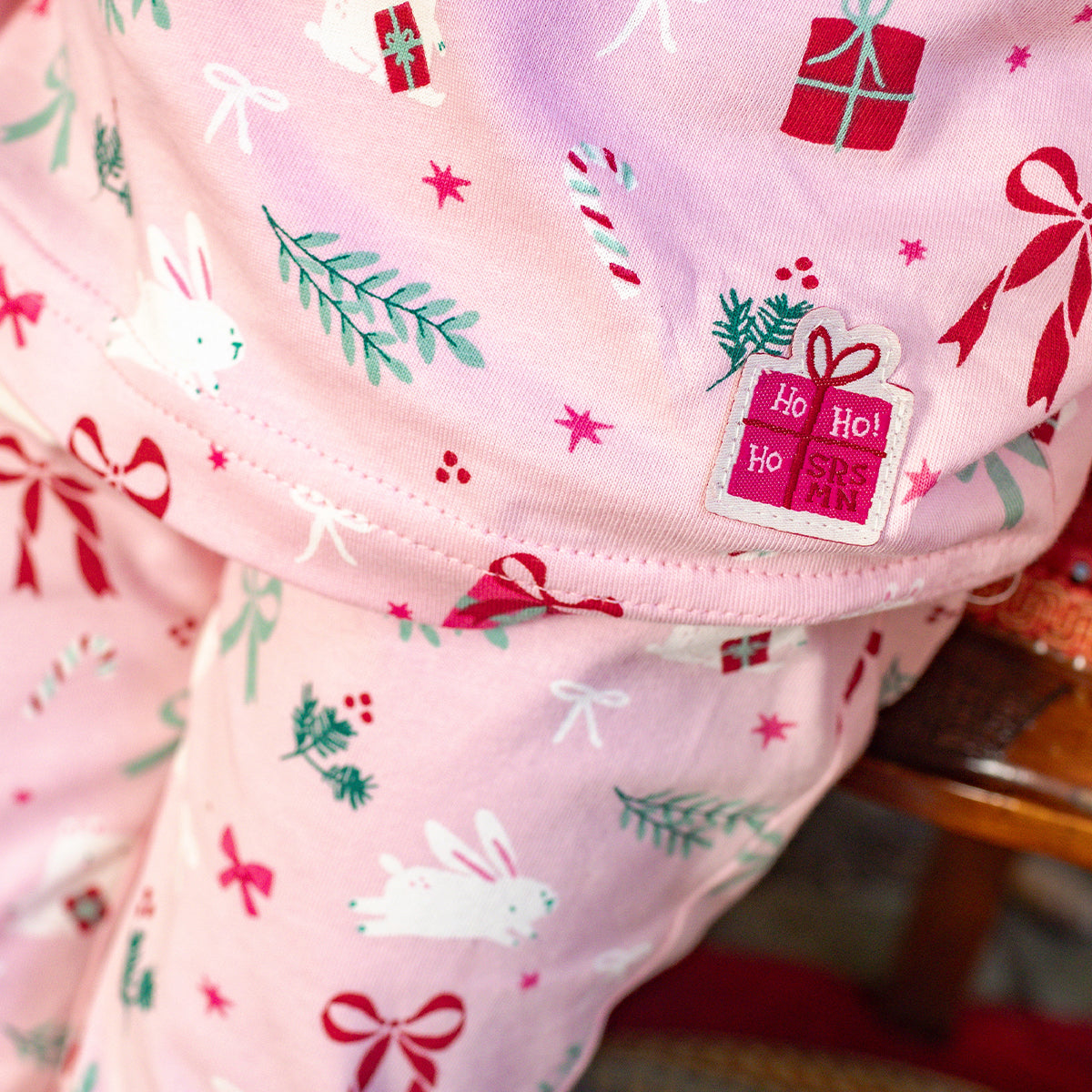 Détail de pyjama rose à motifs des Fêtes avec lapins, cadeaux, rubans et branches de sapin, imprimé sur doux jersey de coton.
