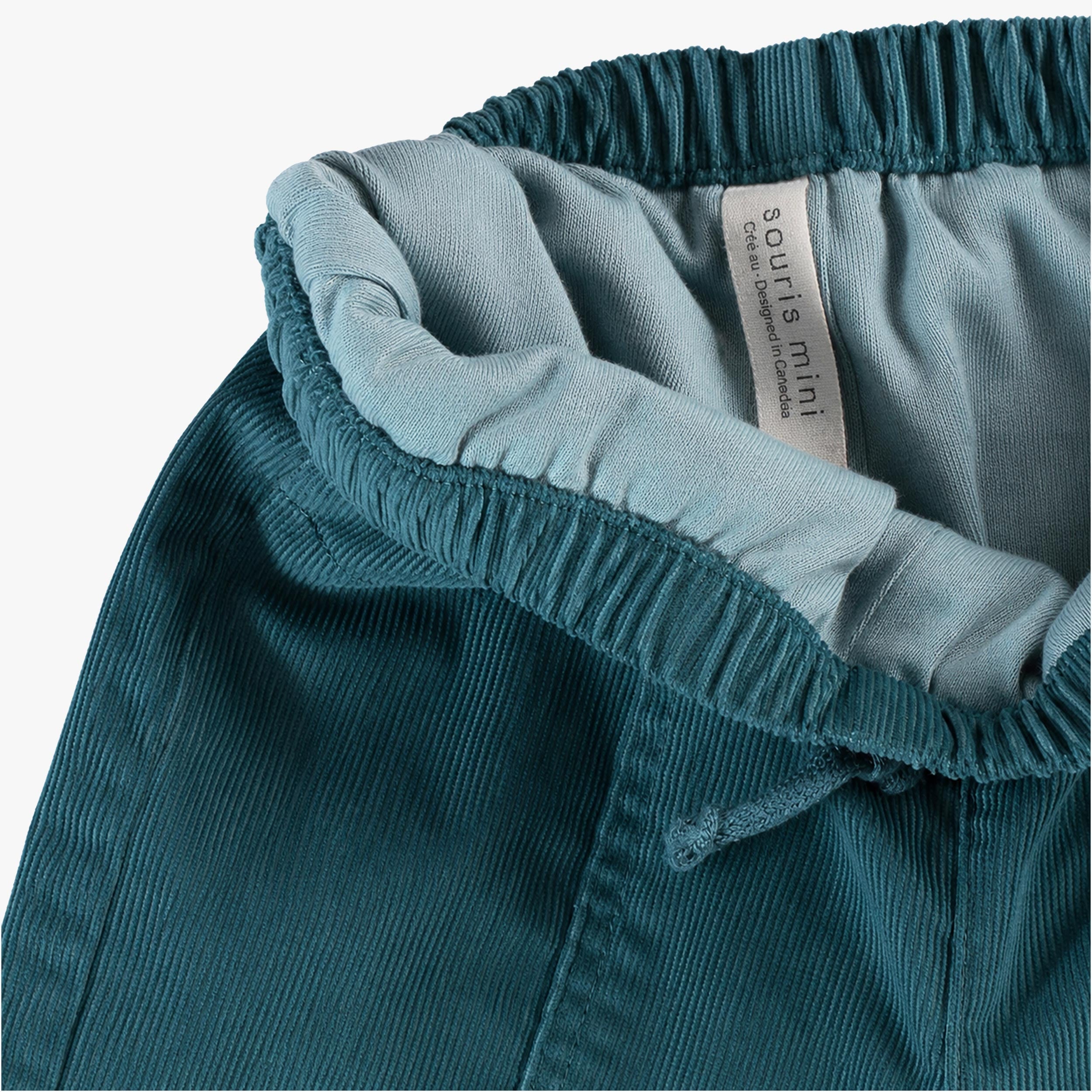 Gros plan sur la taille élastiquée du pantalon bébé bleu pétrole en velours côtelé avec doublure intérieure douce.