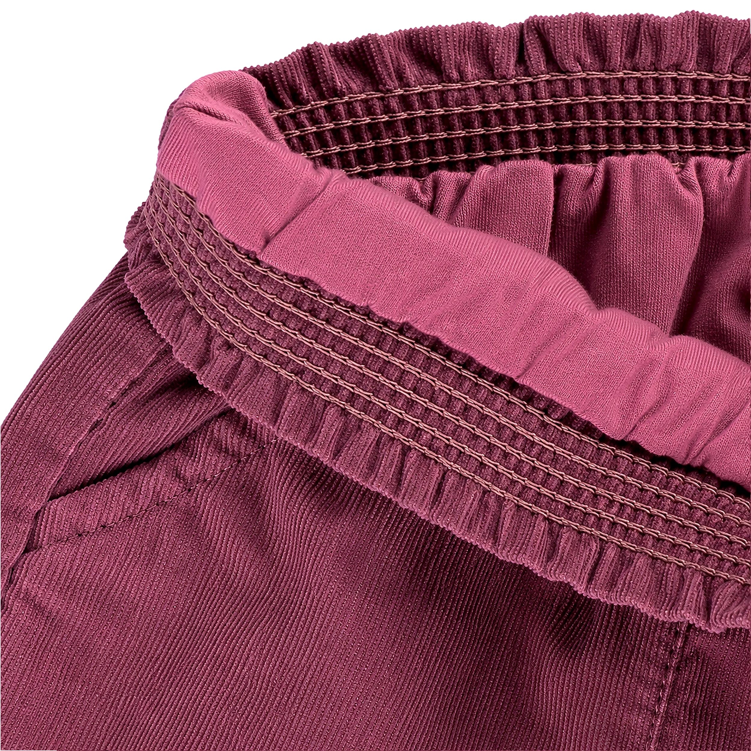 Gros plan sur la taille élastiquée intérieure d’un pantalon bébé fille en velours côtelé prune.