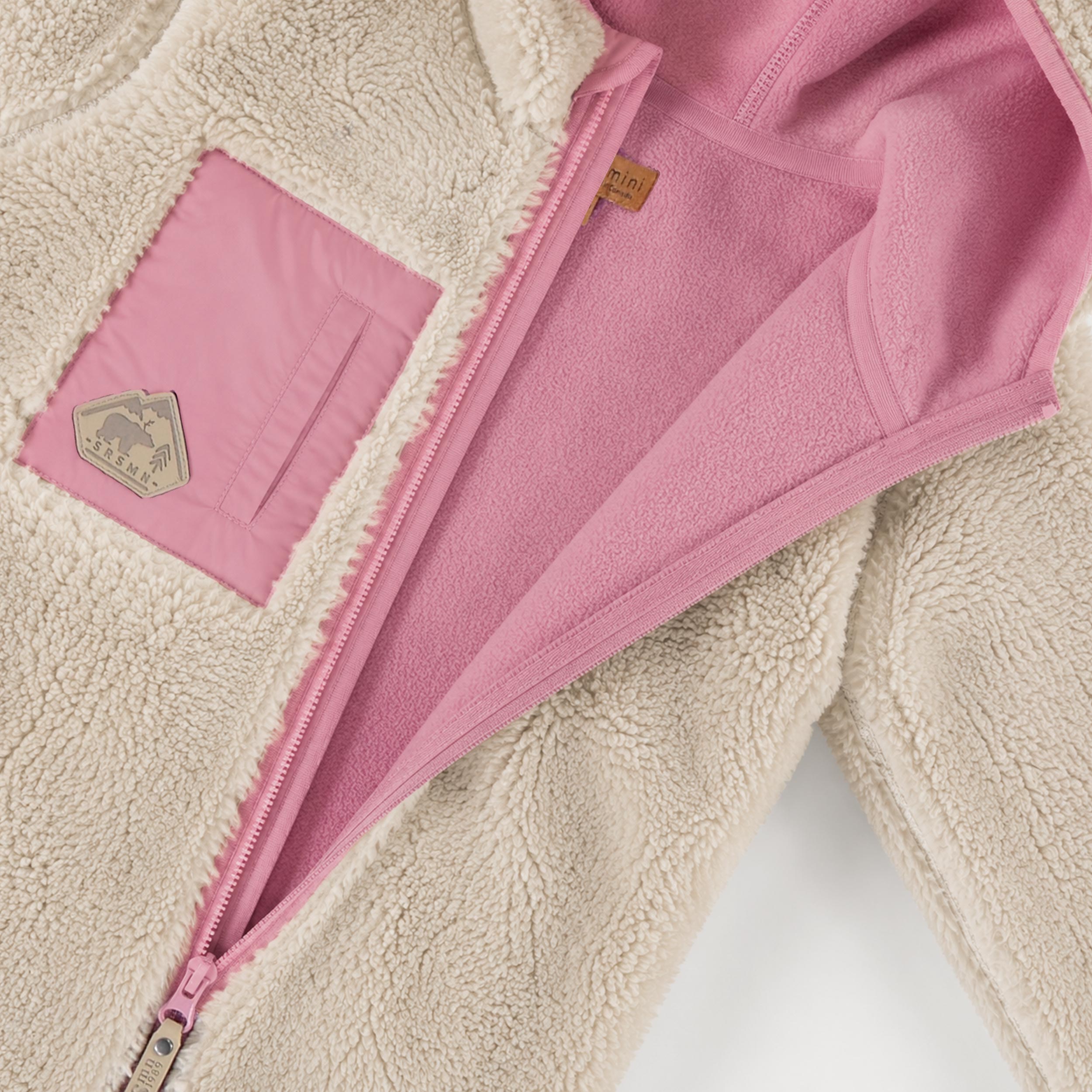 Détail de la doublure polaire rose et de la fermeture éclair de la une-pièce en peluche crème pour bébé.