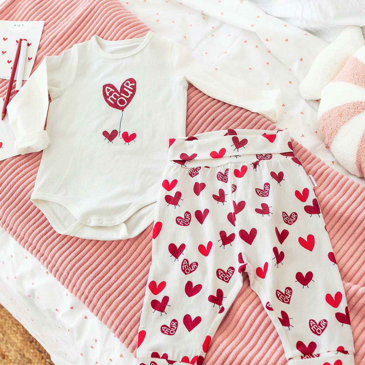 Ensemble bébé Souris Mini composé d’un cache-couche blanc à manches longues et d’un pantalon à motifs de cœurs rouges, présenté à plat.