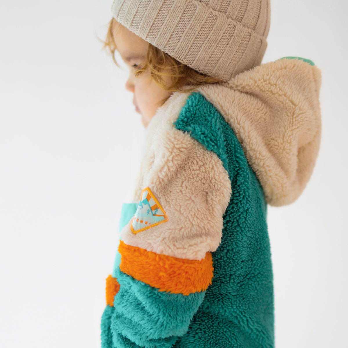 Enfant portant une polaire Souris Mini vert, beige et orange avec capuche, vue de profil arrière.