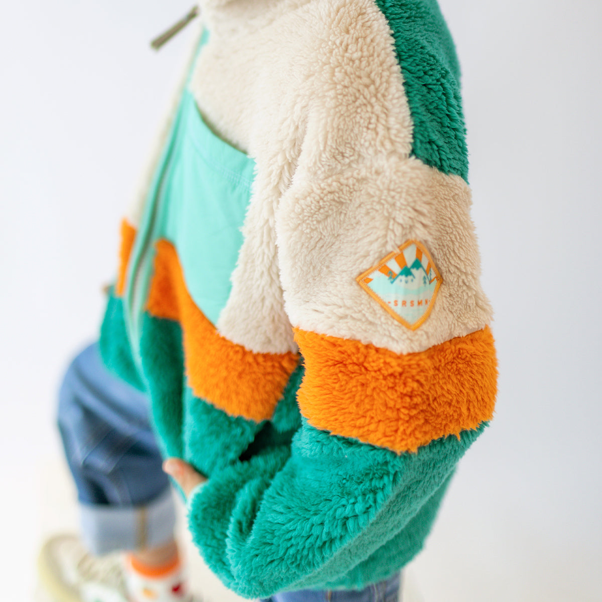 Détail de la manche d’une polaire enfant Souris Mini multicolore, avec écusson brodé et tissu effet peluche.