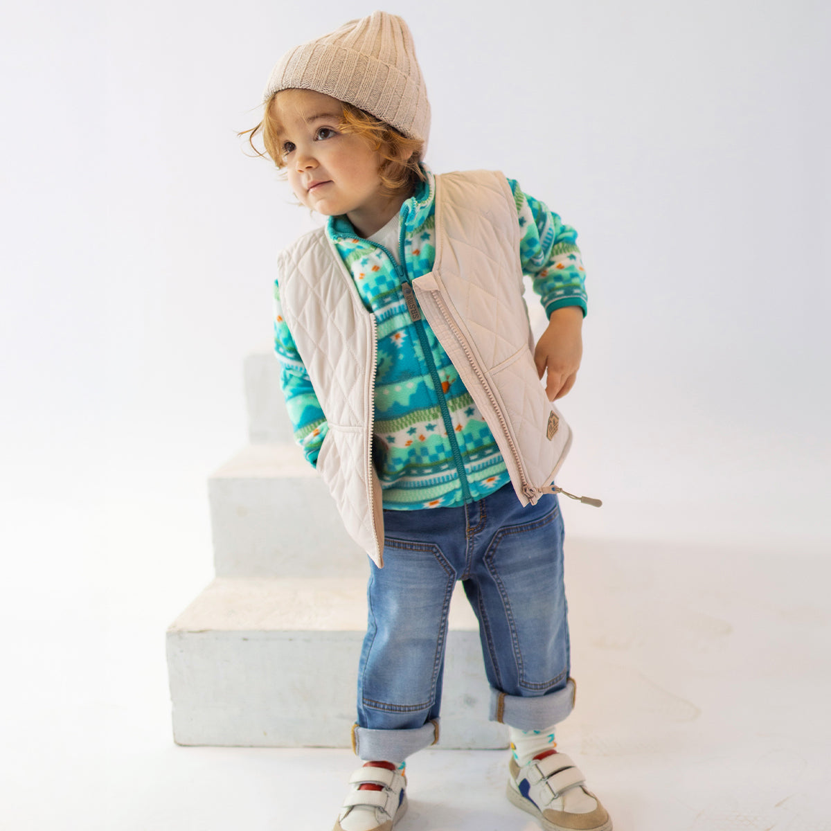 Enfant portant une polaire à motifs verts Souris Mini avec une doudoune sans manches beige.