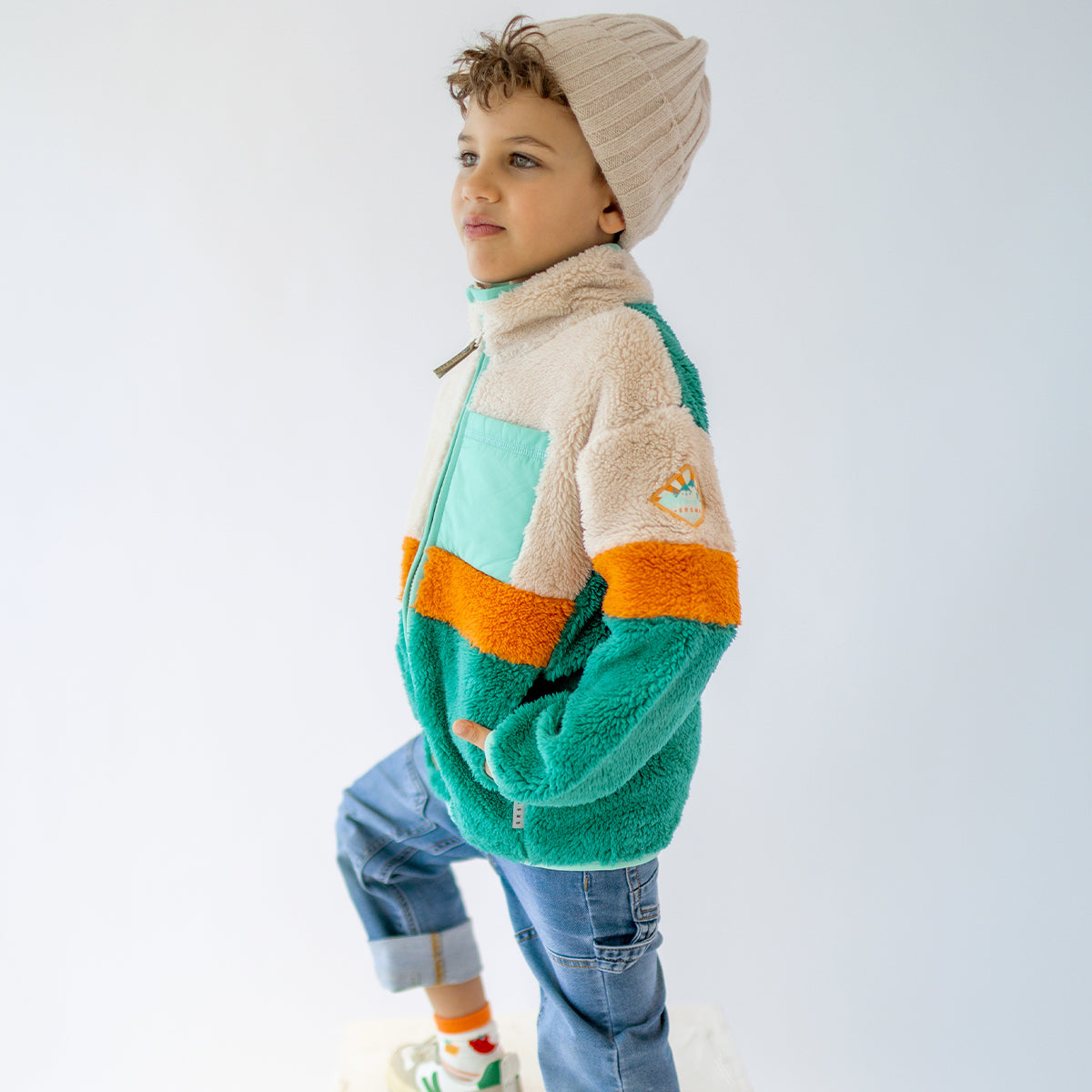 Enfant portant une polaire Souris Mini vert, beige et orange, avec fermeture éclair et poche poitrine, vue de profil.