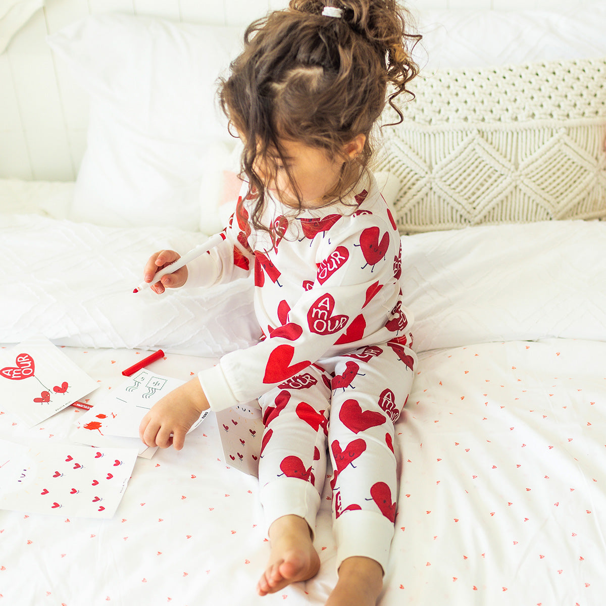  Enfant portant un pyjama blanc à motifs de cœurs rouges Souris Mini, assis sur un lit et dessinant avec des cartes.