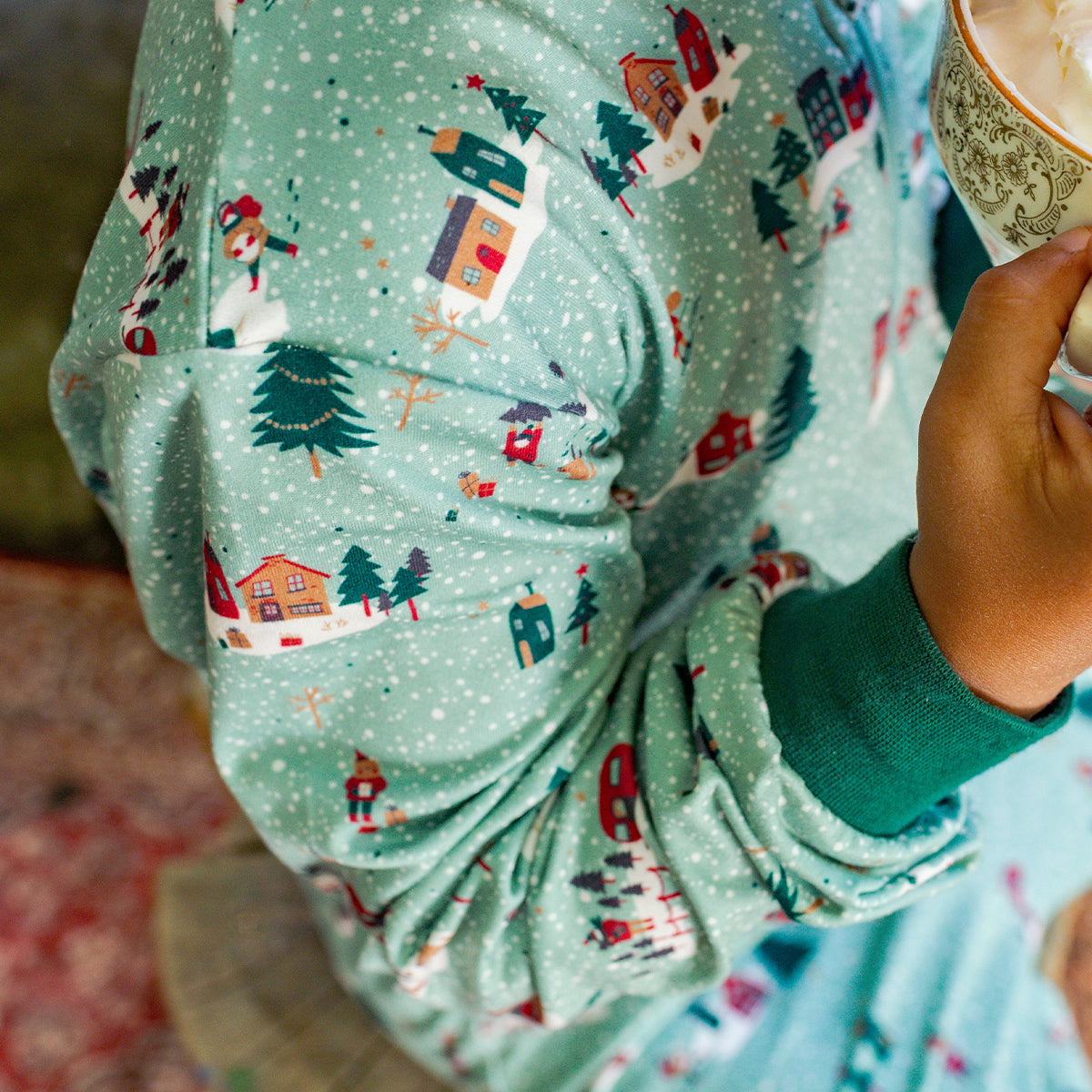 Détail du pyjama vert à motifs hivernaux avec maisonnettes et sapins enneigés, confectionné en tissu doux et confortable.