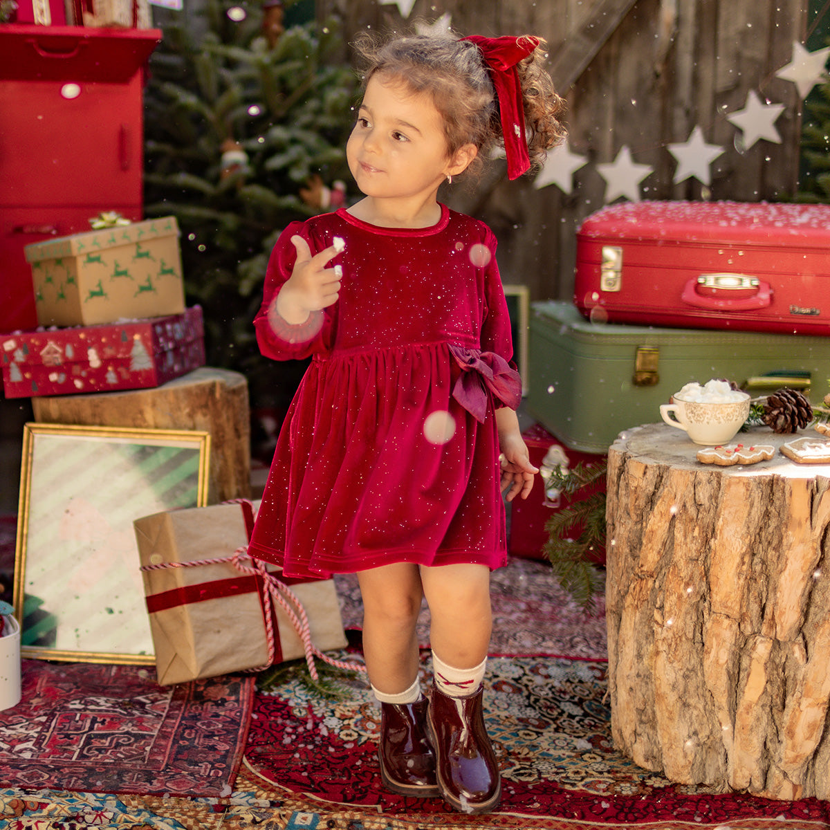 Fillette portant une robe rouge en velours scintillant avec un nœud, debout dans un décor de Noël chaleureux, collection Souris Mini.