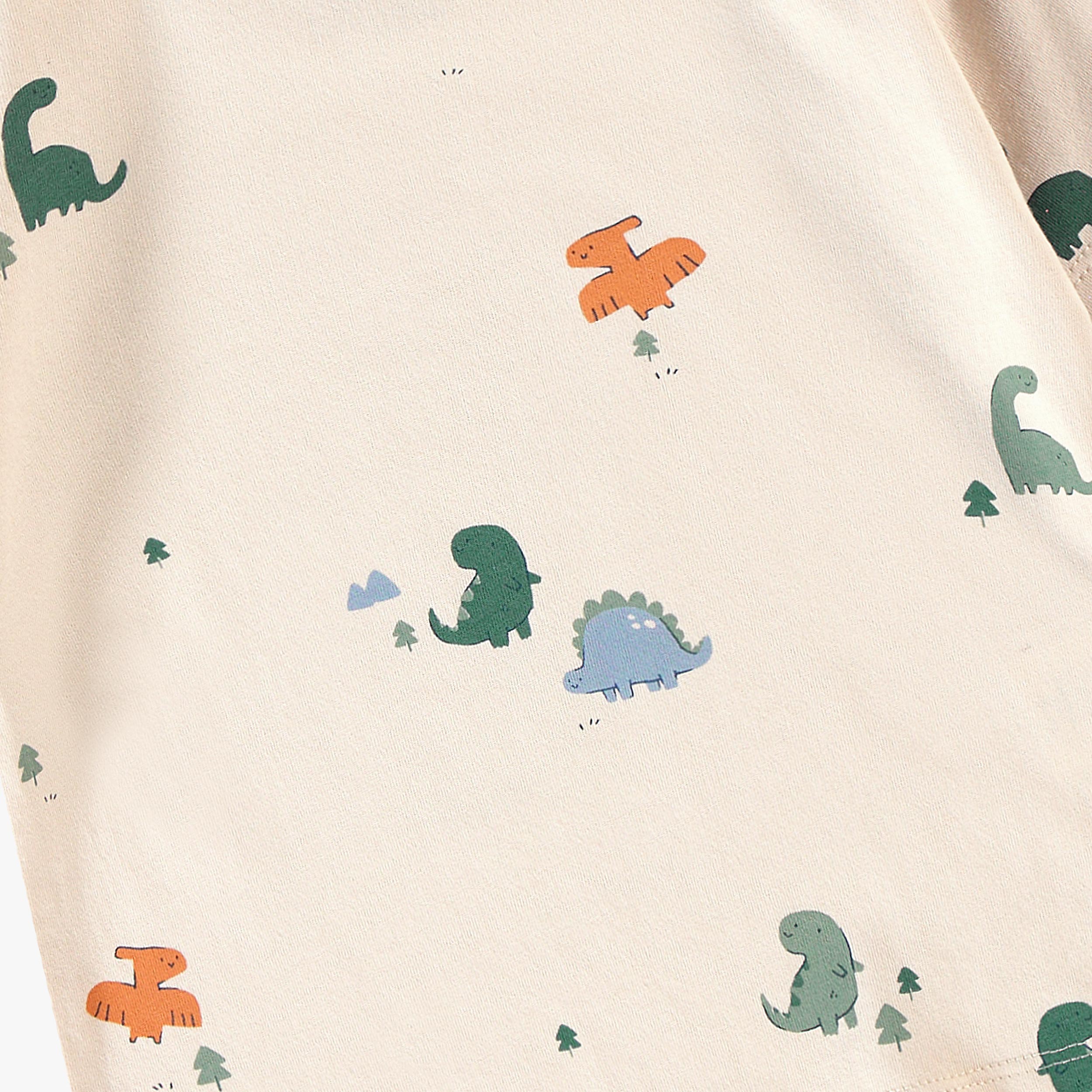 Gros plan sur l’imprimé dinosaures colorés d’un t-shirt bébé écru