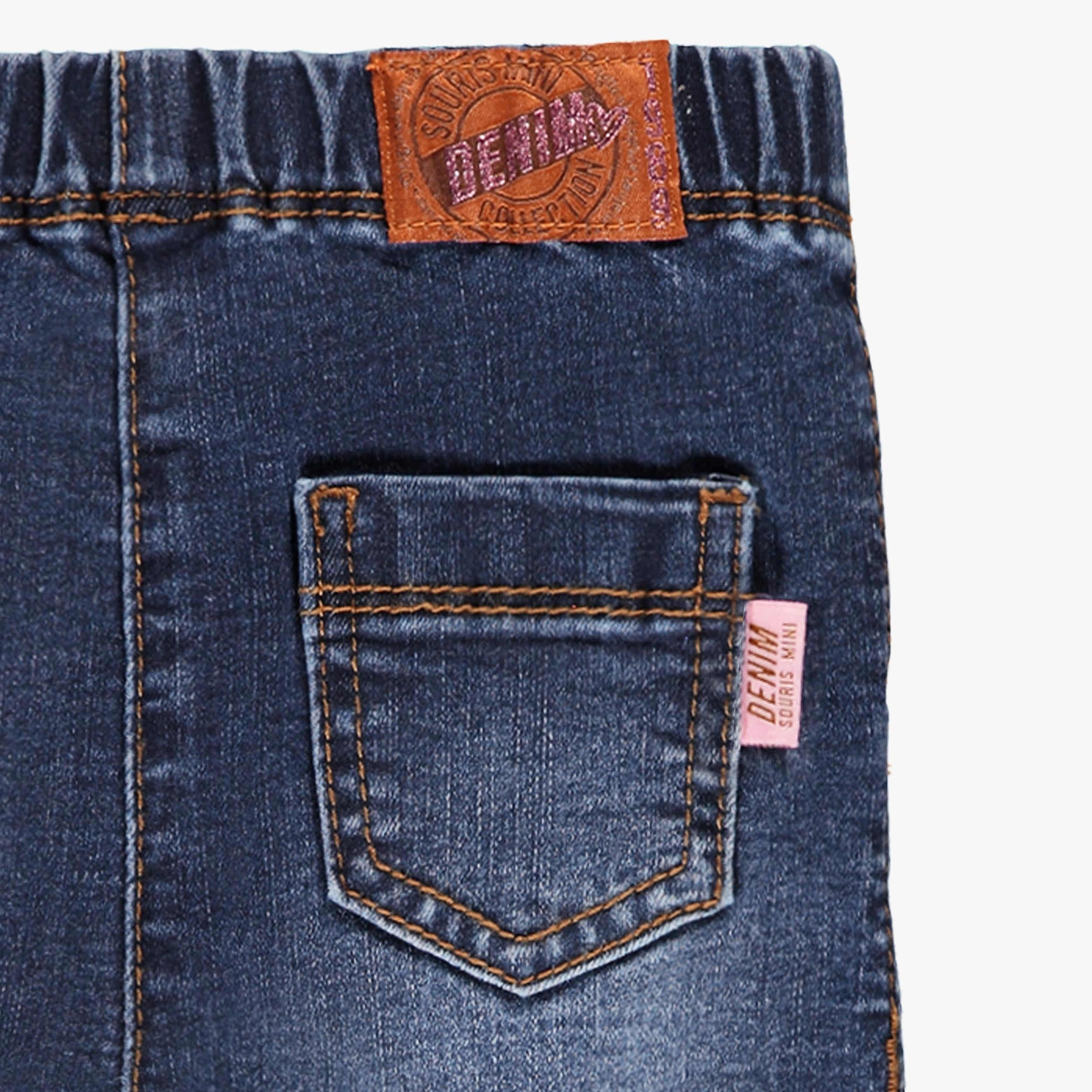Zoom sur la poche arrière d’un jean bébé fille bleu denim avec coutures contrastées