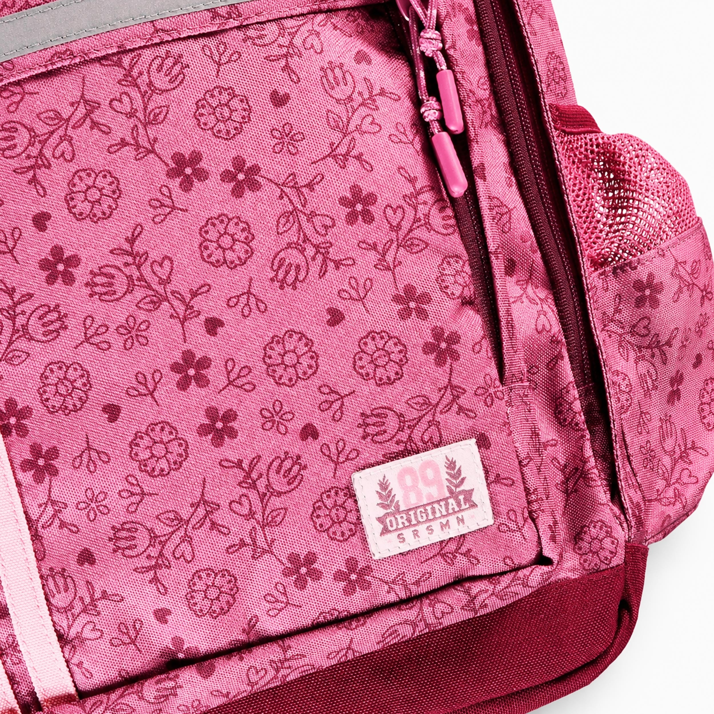 Zoom sur le tissu à motif floral d’un sac à dos enfant rose avec fermeture zippée et poche latérale en filet.