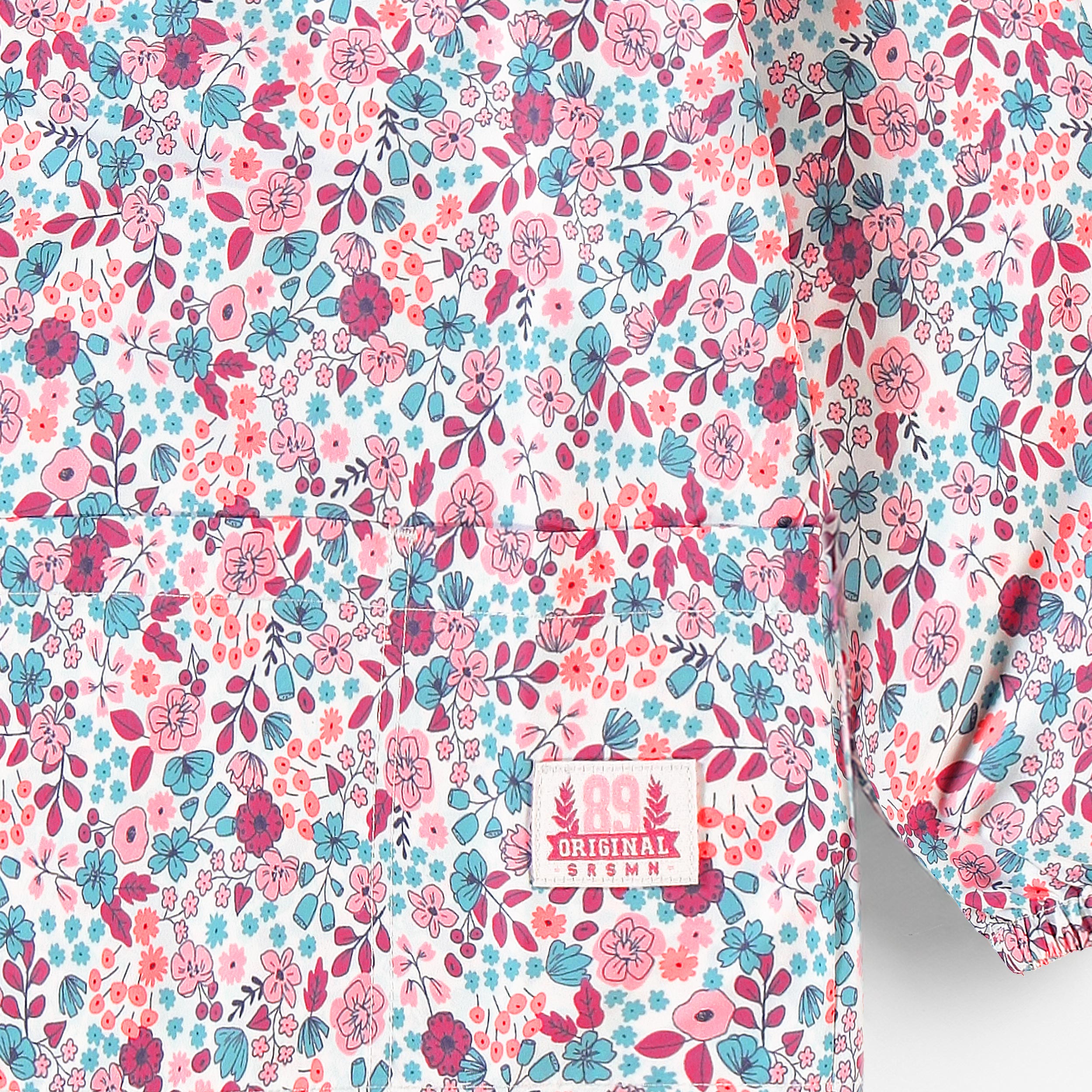Gros plan sur le motif floral coloré d’un tablier de peinture enfant avec poche avant et manches longues.